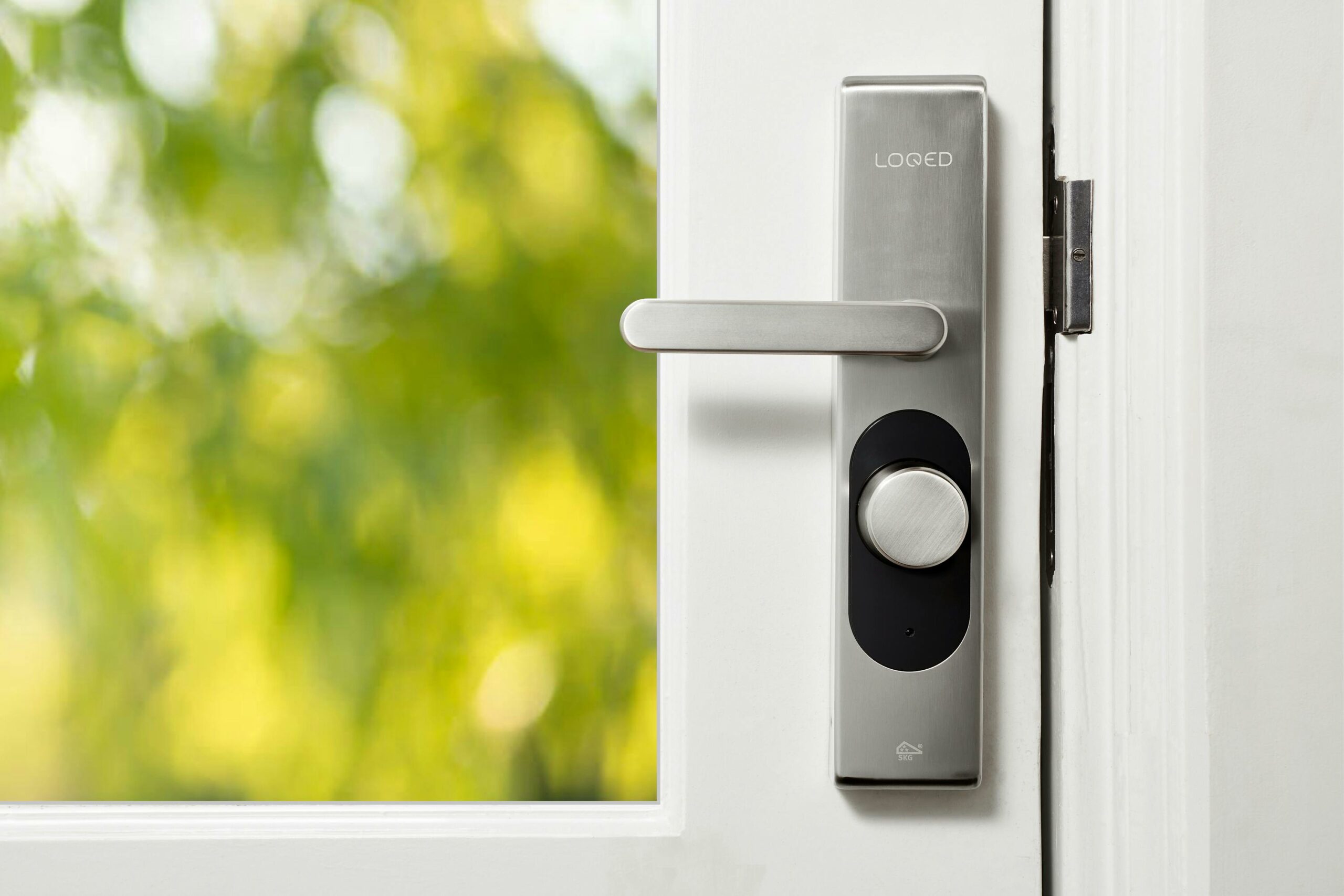 Sleek smart door lock on a white door with blurred green foliage in the background.